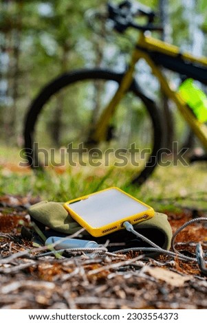 A portable charger charges the smartphone. Power Bank with cable against the background on the forest and bicycle