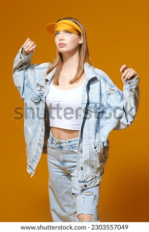Denim youth style. Portrait of a beautiful blonde girl in a denim clothes and a stylish yellow visor on a yellow studio background. Summer fashion. Sportswear. Royalty-Free Stock Photo #2303557049