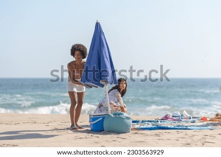 Friends opening the umbrella on the beach, ready to sunbathe.