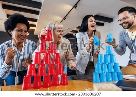 Group of young business people playing, building towers from plastic cups, two teams, blue and red. Teambuilding activity. Royalty-Free Stock Photo #2303606207