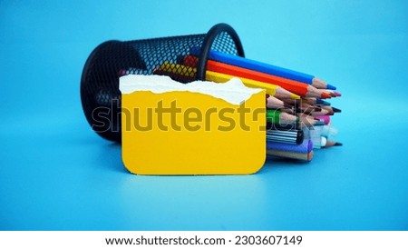 Back to school concept. Front view photo of school supplies, pencils, pens in case and yellow torn paper on isolated blue background with empty space