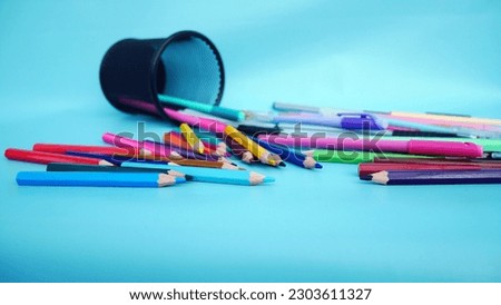 Back to school concept. Front view photo of school supplies, pencils, pens scattering from pencil case on isolated blue background with empty space