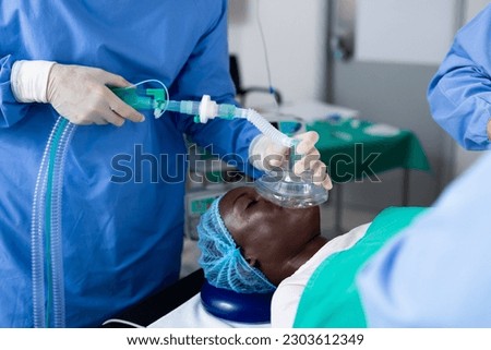 Midsection of surgeon giving african american male patient anesthetic mask in operating theatre. Surgery, hospital, medical and healthcare services. Royalty-Free Stock Photo #2303612349
