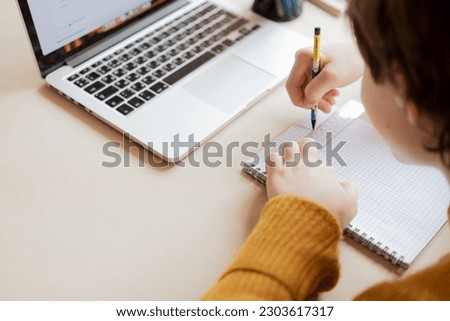 A boy does his school homework with a pencil and ruler in his notebook, top view  Royalty-Free Stock Photo #2303617317
