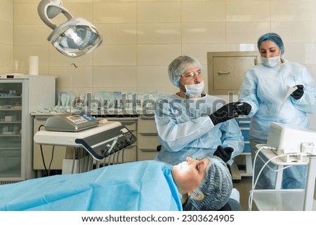 Surgeon and nurse during dental operation. Local anesthetized female patient in surgical room of dental clinic. Installation of dental implants or tooth extraction.  Royalty-Free Stock Photo #2303624905