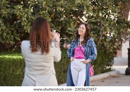 Woman taking a picture of her friend with a mobile phone. Friendship concept.