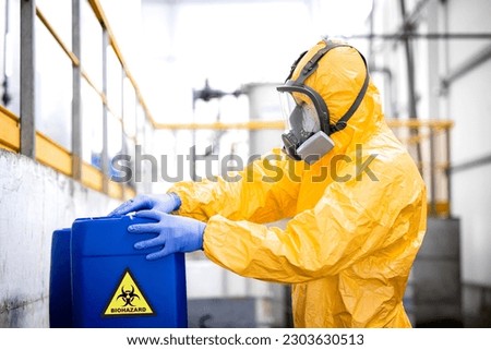 Worker wearing protection equipment and gas mask working in chemicals production factory disposing biohazard waste. Royalty-Free Stock Photo #2303630513