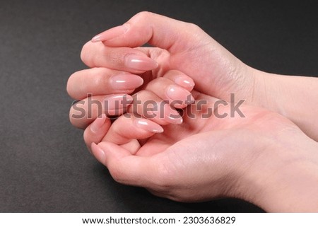 Female hands with pale pink manicure on nails, isolated on black 