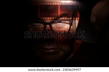 man looks at vintage film in dark room. isolated on black background. Male photograph looking at 35 mm tape. Film photography.  development. vintage hobby.  photo amateur. archive. private detective