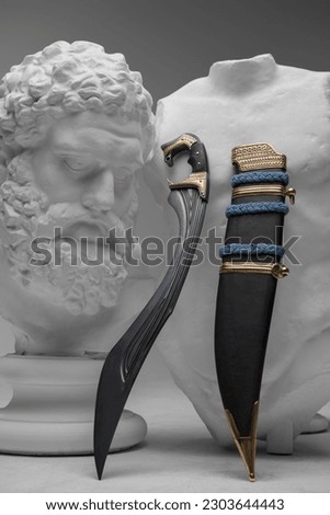 Shot of dagger of soldier against classical bust and chest against gray background. Royalty-Free Stock Photo #2303644443