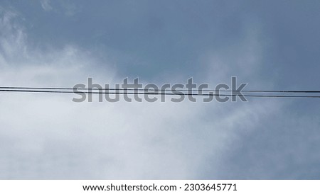 This photo of two electric wires is during a sunny day and the wires have a beautiful blue and white cloud background