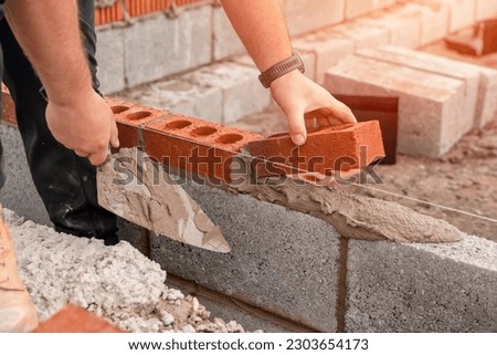 Bricklayer laying brick on cement mix on construction site close-up. Reduce the housing crisis by building more affordable houses concept Royalty-Free Stock Photo #2303654173