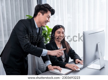 Manager helps female call center operator with customer support. Asian woman call center in headset and microphone gets guidance in modern office. Efficient teamwork for telesales service. Jubilant Royalty-Free Stock Photo #2303693223