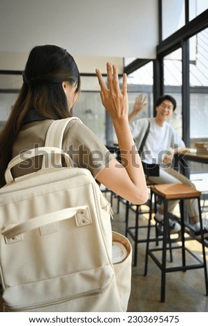 Cheerful asian man student waving hand for greeting to his friend in university campus. Youth lifestyle concept