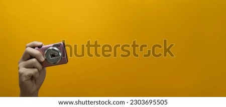 Unrecognizable hand holding old compact camera over yellow background with copy space