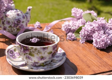 Spring composition with a cup of tea, teapot and lilac flowers on light background. Spring tea party, tea drinking. Menu, greeting card. Side view, copy space for text, product place.