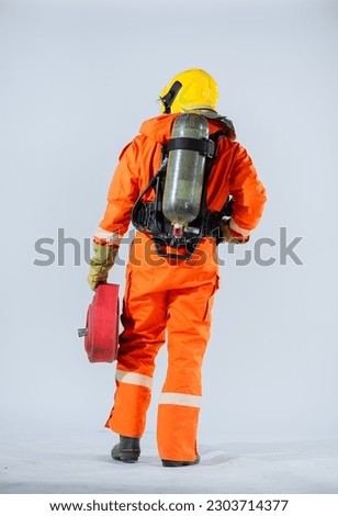 Vertical picture of the firefighter is standing with his back turned on a white background while holding a fire hose.