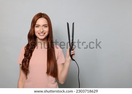 Beautiful woman with hair iron on light gray background, space for text