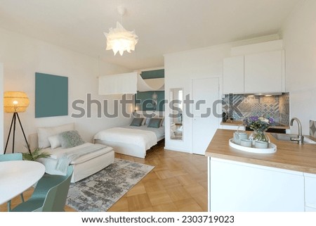 General view of a stylish modern studio apartment. There is a small kitchen with a wooden counter, a double bed and a single bed, and a table with chairs. No one inside