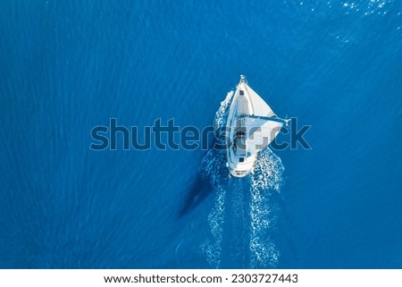 Wave and sail yacht on the sea as a background. 
Sea and waves from top view. Blue water background from top view. Top view from drone. Summertime vacation. Travel image Royalty-Free Stock Photo #2303727443
