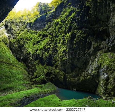shady steep gorge with a lake and an entrance to a cave complex Macocha Royalty-Free Stock Photo #2303727747