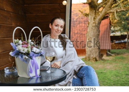 Glad woman wrapped in plaid sitting on terrace with a glass of white wine in the warm evening Royalty-Free Stock Photo #2303728753