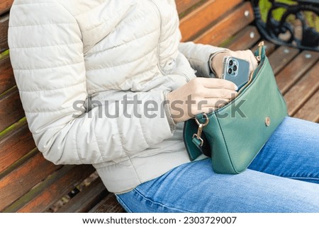 a woman takes a smartphone out of a lady's handbag in the park. girl waiting for a phone call. 