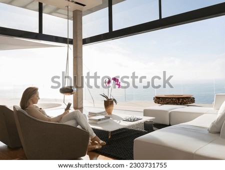 Woman using cell phone in modern living room Royalty-Free Stock Photo #2303731755