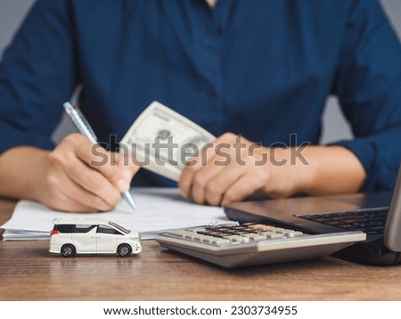Car loan or Title loan. US dollar bills in a hand businessman while sitting at the table. Miniature a red car model, a calculator, and a laptop on a table. Car finance and insurance concept Royalty-Free Stock Photo #2303734955