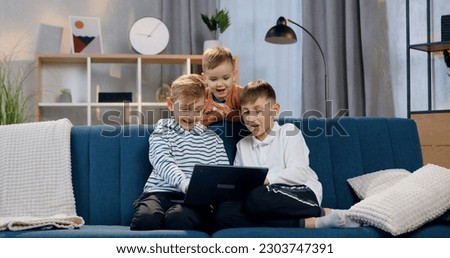 Close up of cute happy smiling three boys which sitting on the comfortable couch and watching interesting programm on computer