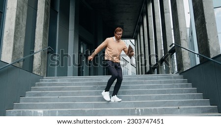 Happy young man actively dancing while walking down the stairs. Cheerful man walks on stairs outside his office, starts funny victory dance celebrating. Royalty-Free Stock Photo #2303747451