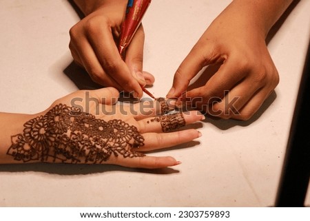Young Teen Age Indian Girl painting henna Tattoo on the hand.