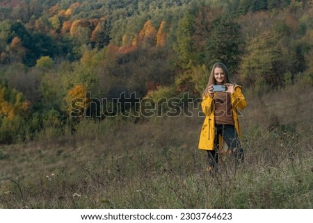 Girl in yellow jacket photographe of autumn nature. Young woman with smartphone, forest on background