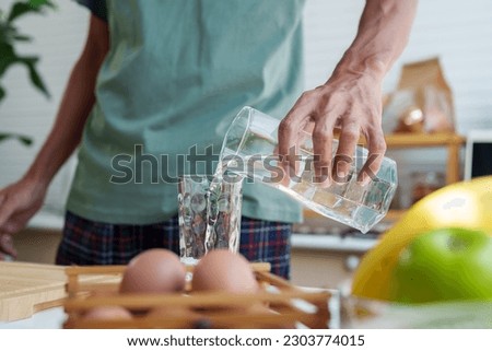Close-up man's hands, handle pitcher, pouring clean water from pitcher into glass, in sufficient quantities drink in order drink it all in one go, after pouring, bring pitcher back its original place. Royalty-Free Stock Photo #2303774015