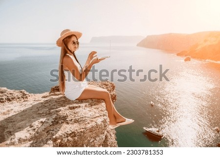 Woman laptop sea. Working remotely on seashore. Happy successful woman female freelancer in straw hat working on laptop by the sea at sunset. Freelance, remote work on vacation