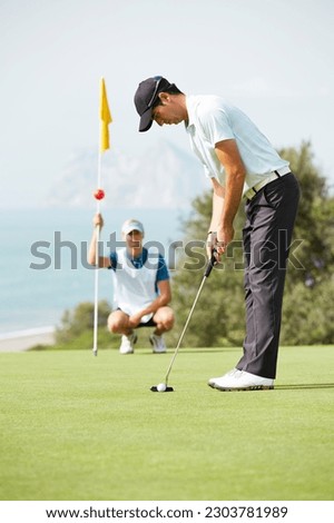 Caddy watching man putt on golf course Royalty-Free Stock Photo #2303781989