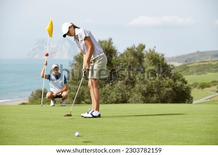 Caddy watching woman putt on golf course Royalty-Free Stock Photo #2303782159