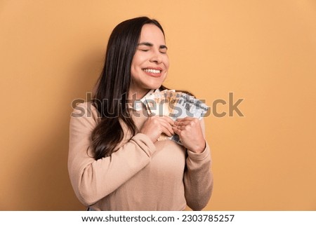 fun brunette young woman celebrating successful business money in all beige colors. business, loan, pay, wealth concept. Royalty-Free Stock Photo #2303785257