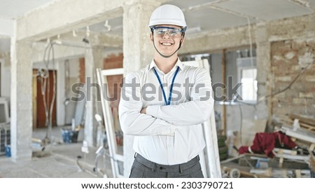 Young hispanic man architect smiling confident standing with arms crossed gesture at construction site
