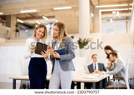 Two pretty young business women looking at financial results on digital tablet in front of their team at the office Royalty-Free Stock Photo #2303790757