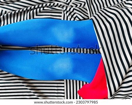 blue tights. female legs in blue tights sit on a black and white striped fabric with a red detail. female knees Royalty-Free Stock Photo #2303797985