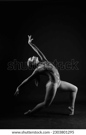 Flexible girl, rhythmic gymnastics artist jumping on white dark background. Grace in motion, action.