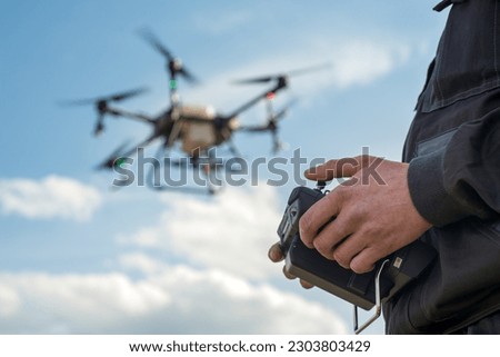 a farmer with a remote control in his hands for spraying with an agrodrone in sky, the latest fertilizer application technologies, focus on hands Royalty-Free Stock Photo #2303803429