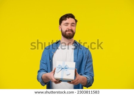 Young man with a gift in his hands. Male model in a blue shirt on a yellow background. Emotions, advertisement concept