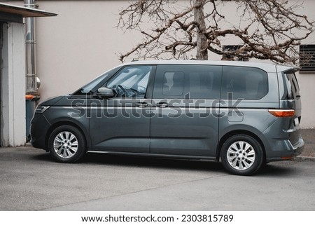 A grey travel van parked in a parking lot next to the private house. Family car for the road trips along the ocean coast. Royalty-Free Stock Photo #2303815789