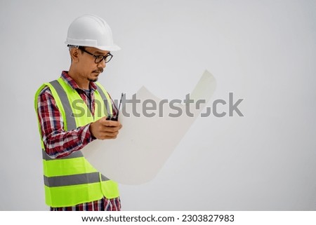 Portrait of an Asian Male Engineer in a white Hard hat Looking up Blueprints on a Piece of Paper with an Isolated White Background.