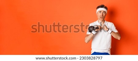 Concept of workout, gym and lifestyle. Close-up of weak and slim middle-aged fitness guy, doing sport exercises with kettlebell, standing over orange background.