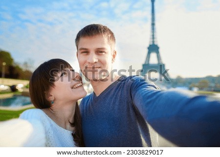 Young romantic couple having a date and taking funny wide angle selfie with mobile phone near the Eiffel tower in Paris, France