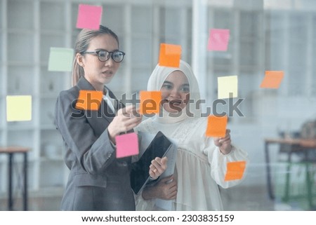 Two Asian businesswomen holding a note on the board, presenting about financial business.