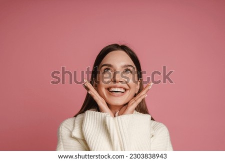 Young cheerful woman wearing sweater looking upward while posing isolated over pink studio wall Royalty-Free Stock Photo #2303838943